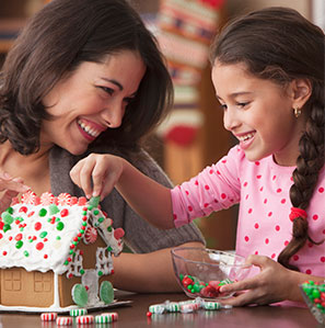 Mom and daughter after using DialCare smiling decorating gingerbread house on kitchen table