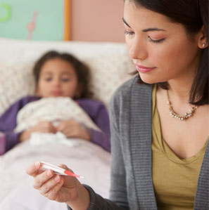 Mom on edge of daughter's bed, while she's under covers, checking her thermometer