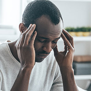 Man sitting forward rubbing temples due to a migraine