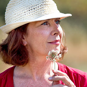 Older woman after using DialCare smiling in field with sunhat smelling flower in hand