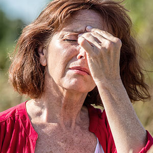 Older woman in field in discomfort rubbing between eyebrows with fingers